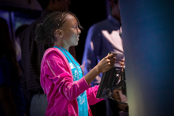 A child smiles as they hold an interactive tablet in the museum.