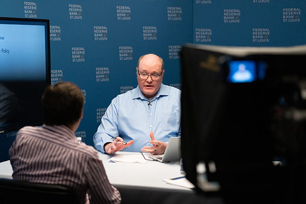Two economists in discussion in a video studio, at a table.